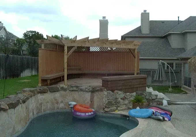 Backyard pool with a wooden deck and two colorful inflatable rafts beside a stone retaining wall