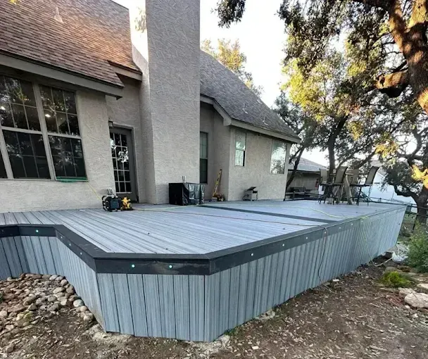 Raised gray deck attached to a house, with black trim and slanted sides in a yard.