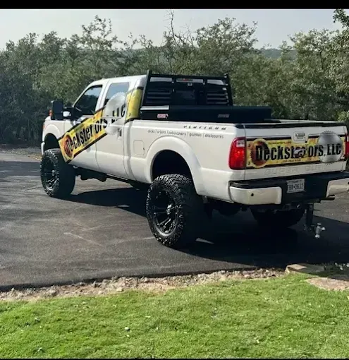 White lifted pickup truck with company decals parked on a driveway beside grass and trees