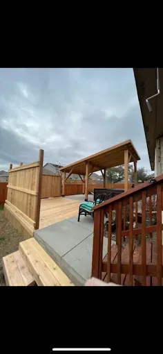 Wooden backyard deck with a covered pergola, ramp, and railing under a cloudy sky