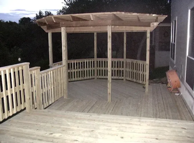Backyard wooden deck with railing and pergola at dusk