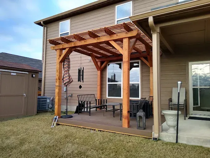 Back patio with wooden pergola, outdoor seating, and a small grill beside a beige house