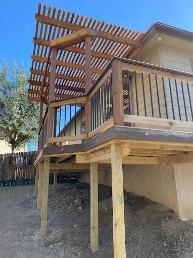 Backyard deck under construction with wooden posts, railing, and pergola against a house
