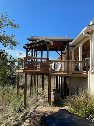 Wooden deck and pergola overlooking dry hillside under a clear blue sky