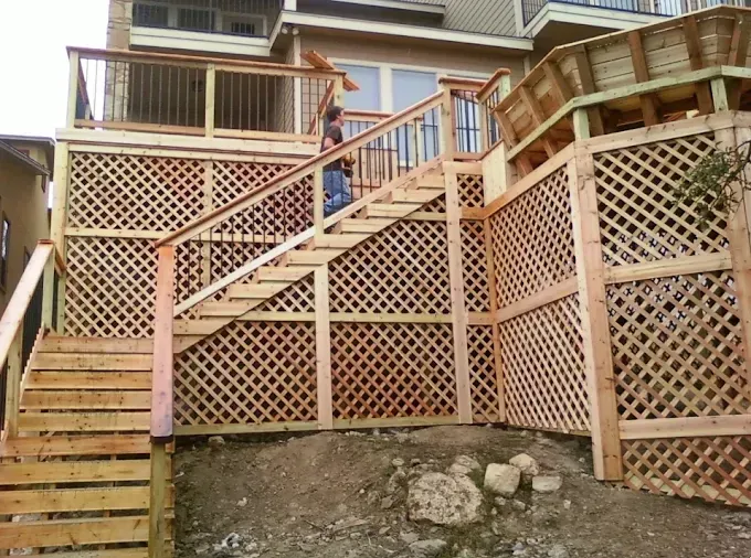Wooden lattice deck and stairs on a house, with a person standing on the upper landing.