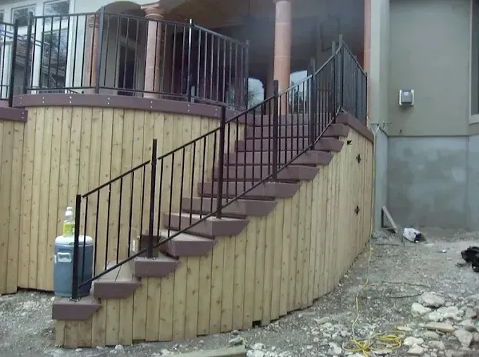 Outdoor staircase with black railings beside a wooden retaining wall and house entrance