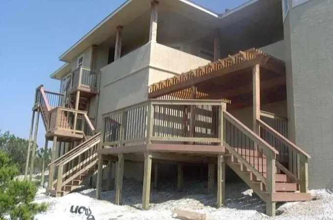 Outdoor wooden deck and stairs attached to a beige house under construction
