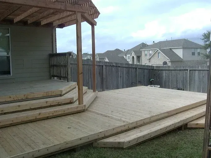 Wooden backyard deck with stairs and a covered porch beside a fenced suburban yard