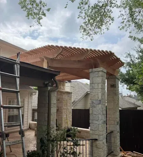 Stone patio pergola under construction with a terracotta roof and metal ladder beside it