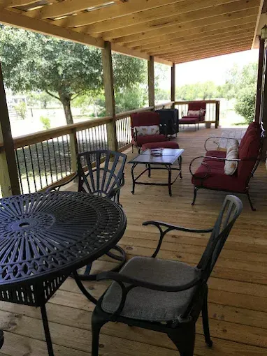 Covered porch with black metal patio furniture and a red cushioned bench overlooking a grassy yard