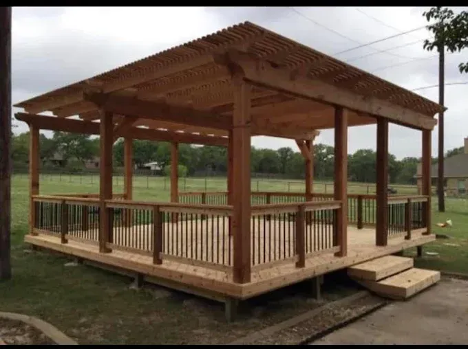 Wooden pavilion with a roof and railing on a raised foundation in a grassy field