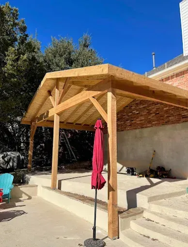 Wooden patio pergola with a red umbrella beside concrete steps under a clear blue sky