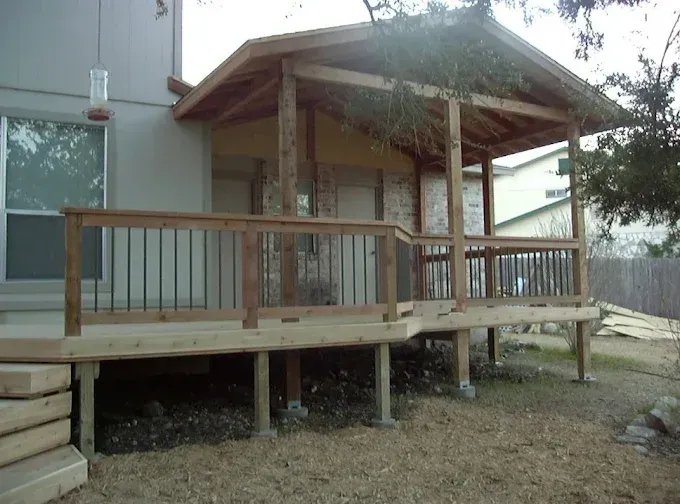 Wooden porch with railing and steps beside a house in a yard