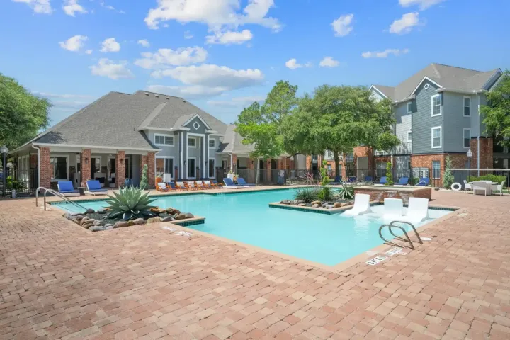 Swimming pool at an apartment complex, blue water, brick patio, blue building, blue sky, trees.