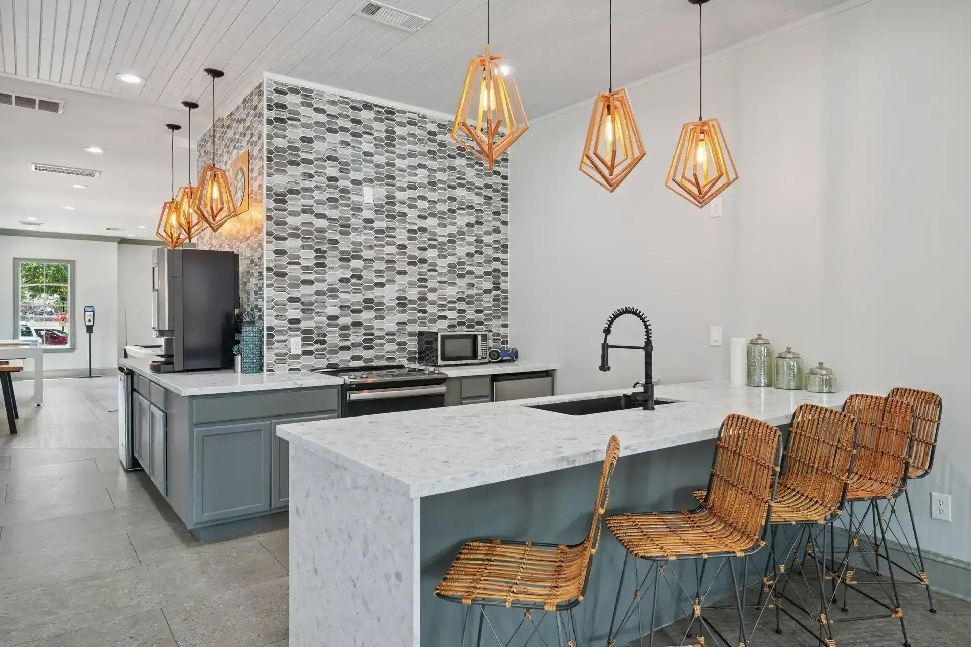 Modern kitchen with a white quartz countertop island, woven bar stools, and geometric pendant lights.