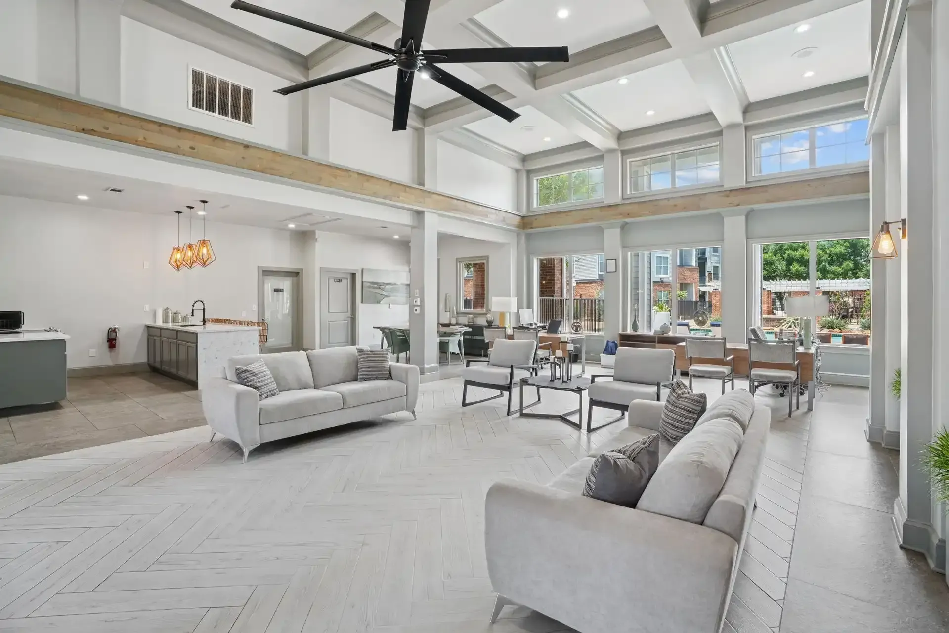 Spacious, light-filled room with couches, chairs, and a large ceiling fan; windows offer views of the outdoors.