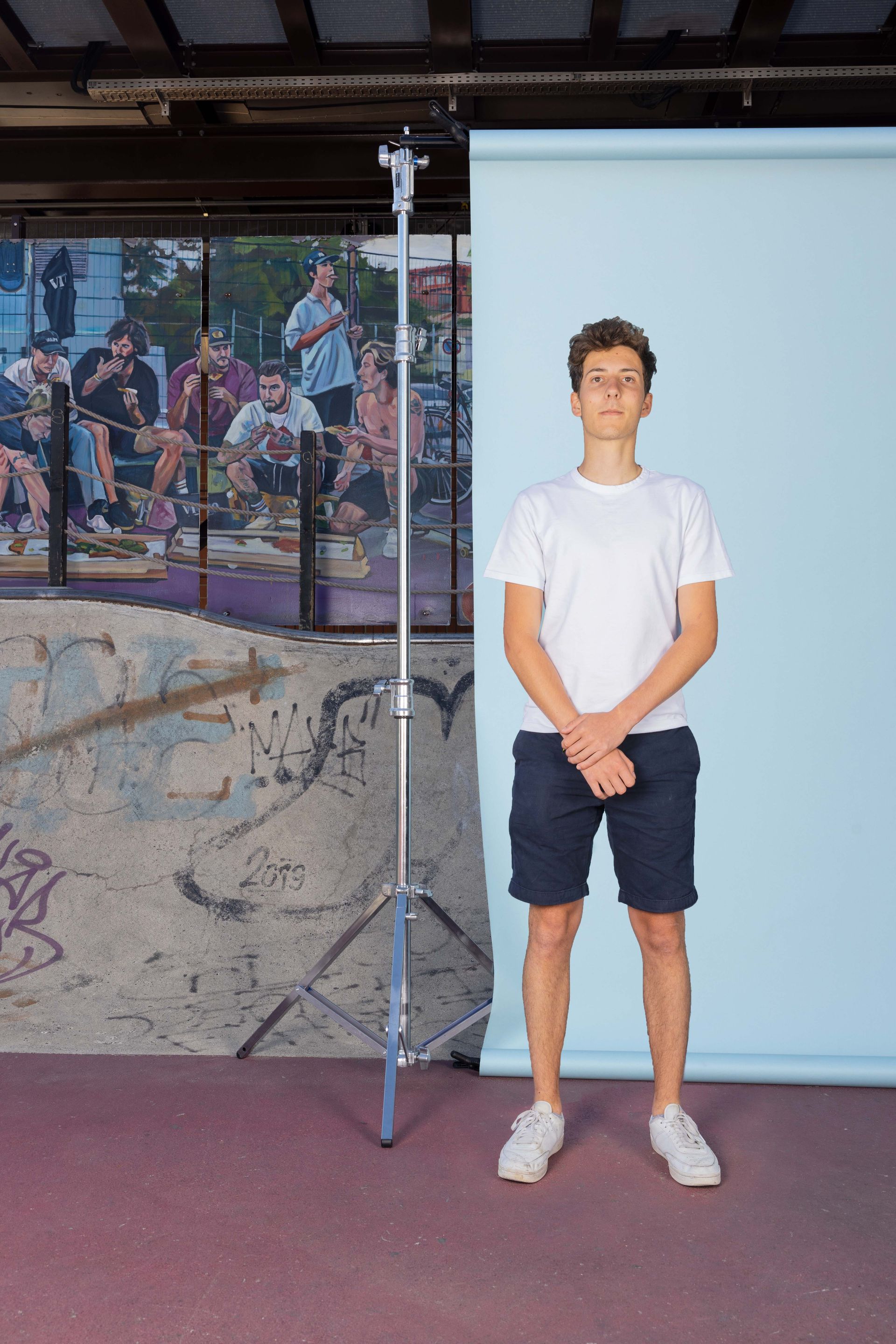 Ein junger Mann in einem weißen T-Shirt und Shorts steht vor einem blauen Hintergrund.