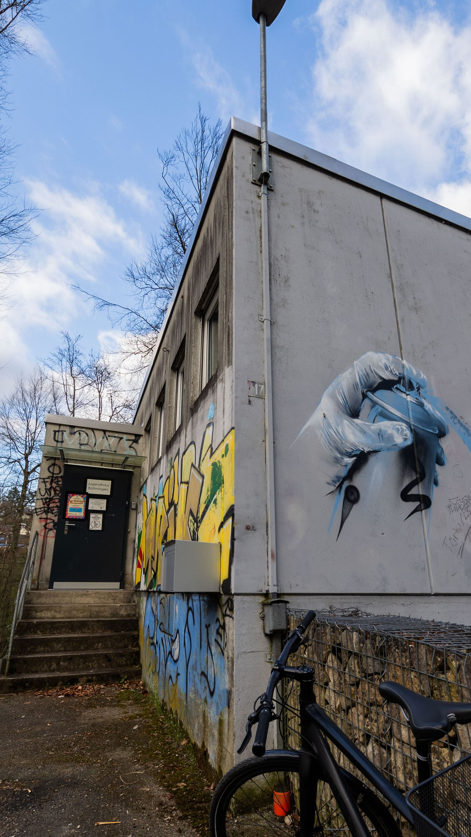 Gebäude mit Graffiti, davor ein Fahrrad und Stufen, die zu einem dunklen Eingang führen.