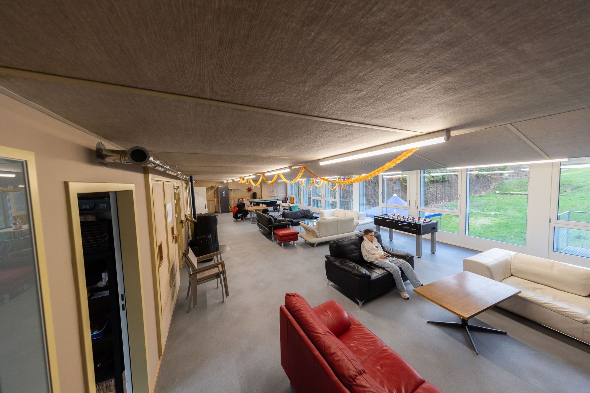 Jugenhaus mit Sofas, Tischen und großen Fenstern, dargestellt in einer leicht geneigten Weitwinkelansicht