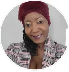 Woman with a maroon hat and plaid blazer smiles, looking at the camera.