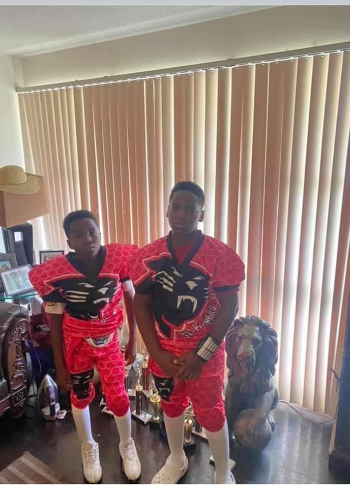 Two boys in red and black football uniforms pose indoors, with a lion statue nearby.