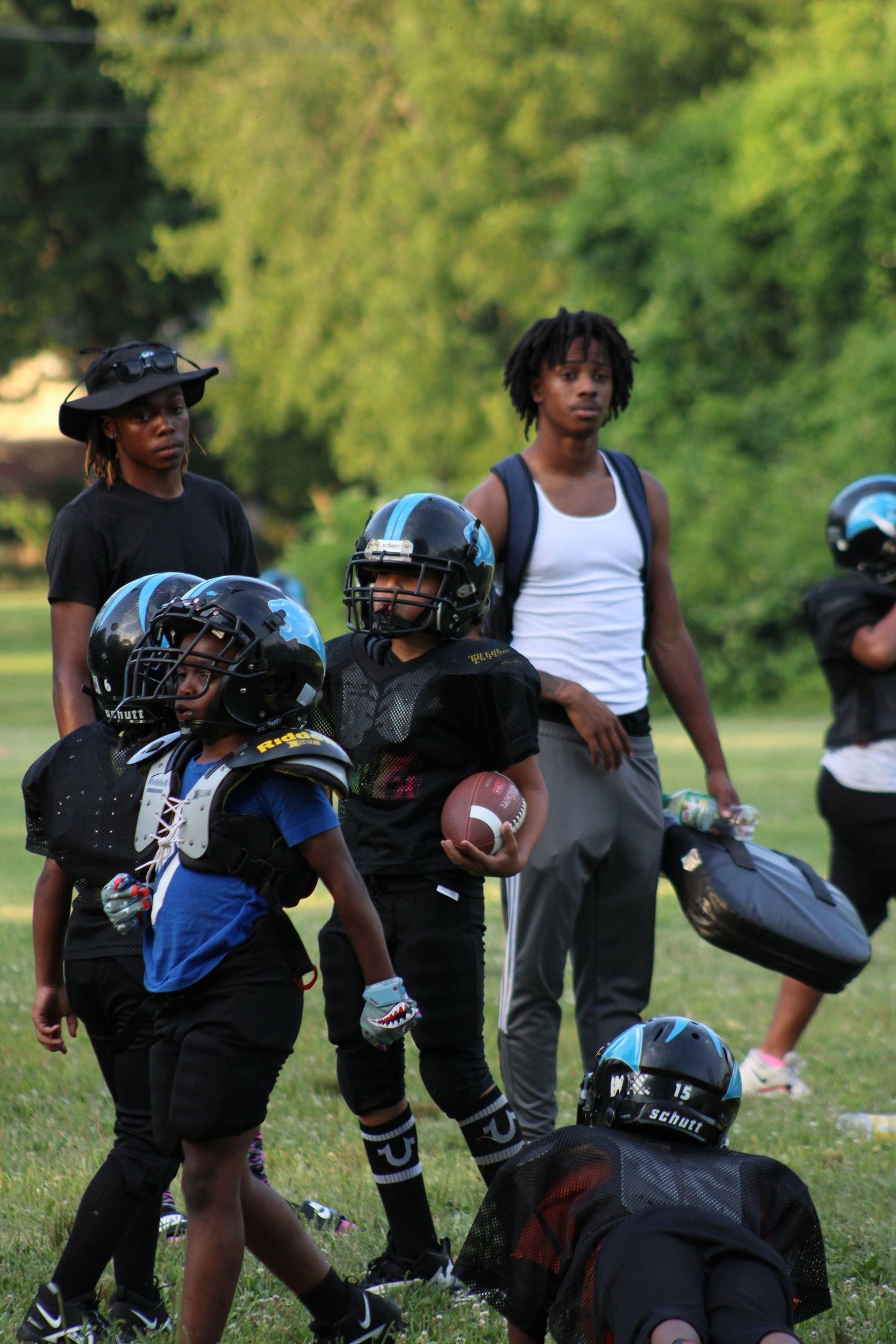 Youth football players and coach on a grassy field. Kids in helmets, one holding a football.