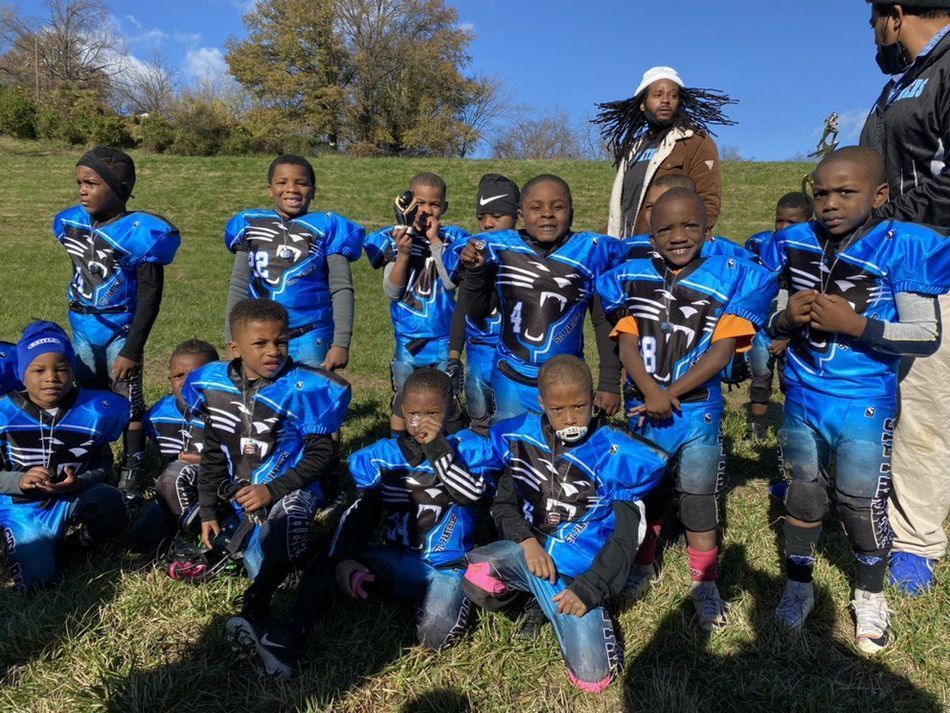 Youth football team in blue uniforms poses on a grassy field, smiling.