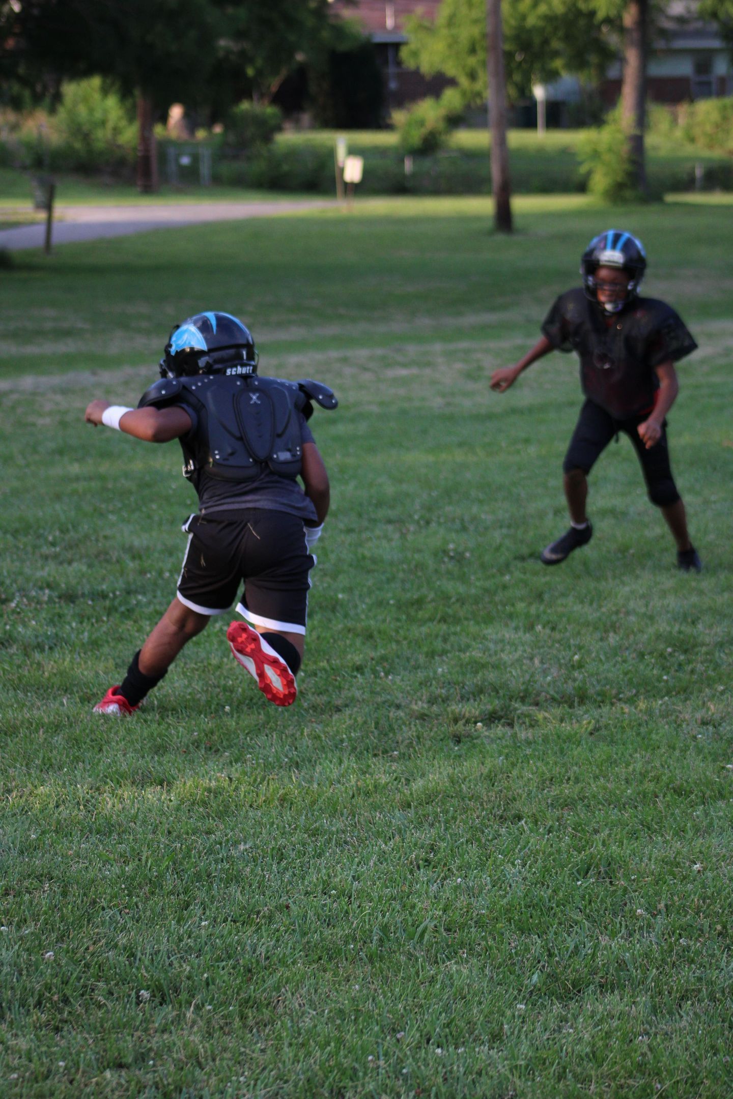 Two young boys playing football on a grassy field, one running with the ball, the other defending.