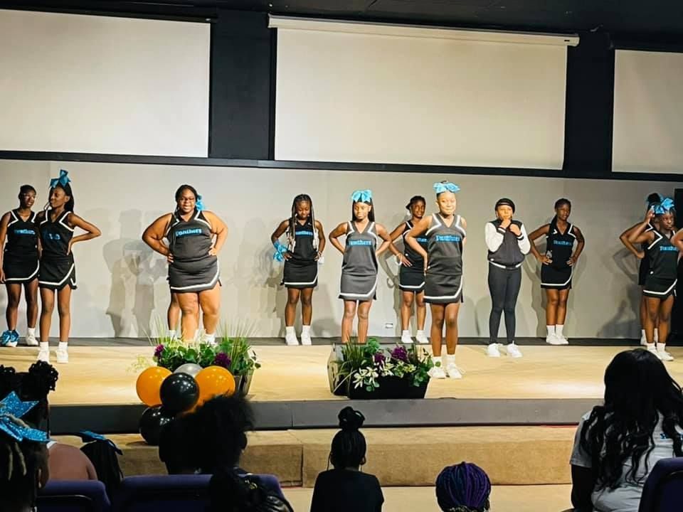Cheerleaders in blue/black uniforms on stage; a crowd watches.