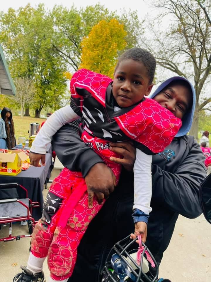 A woman holds a young boy in football gear outside. The boy looks at the camera.