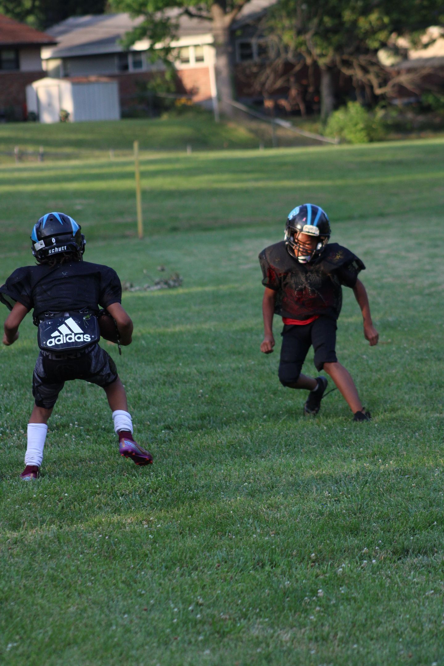 Two young football players in black uniforms on a grassy field; one holds a ball.