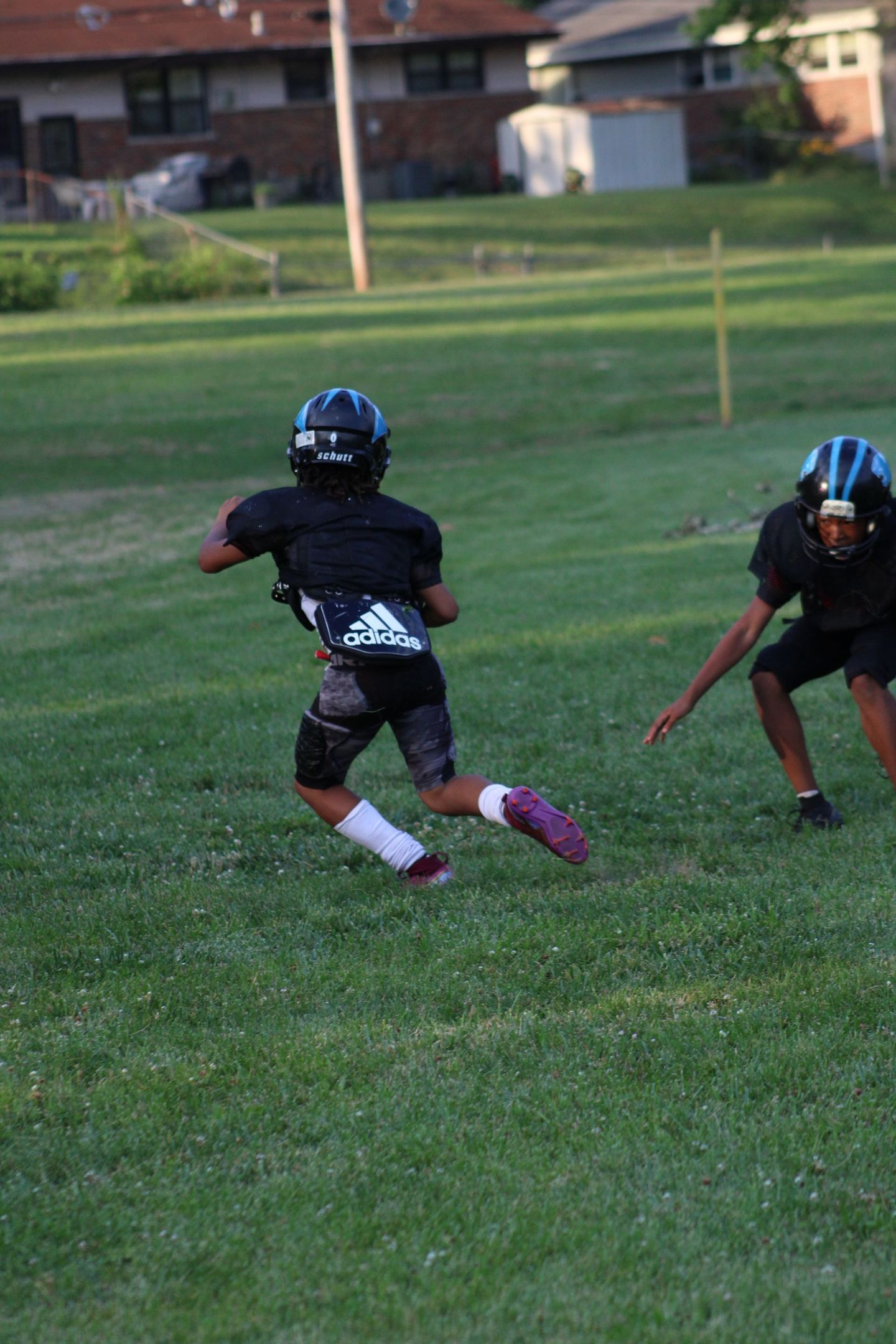 Two young football players in black uniforms run on a grassy field.