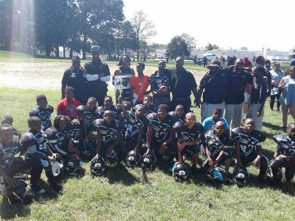 Youth football team posing for a group photo on a grassy field. The team is in black uniforms.