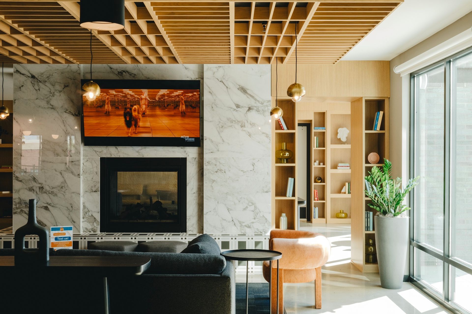Cozy living room with fireplace, TV, built-in shelving, and large window. Features a modern design with marble and wood accents at Revelry in Madison, WI.