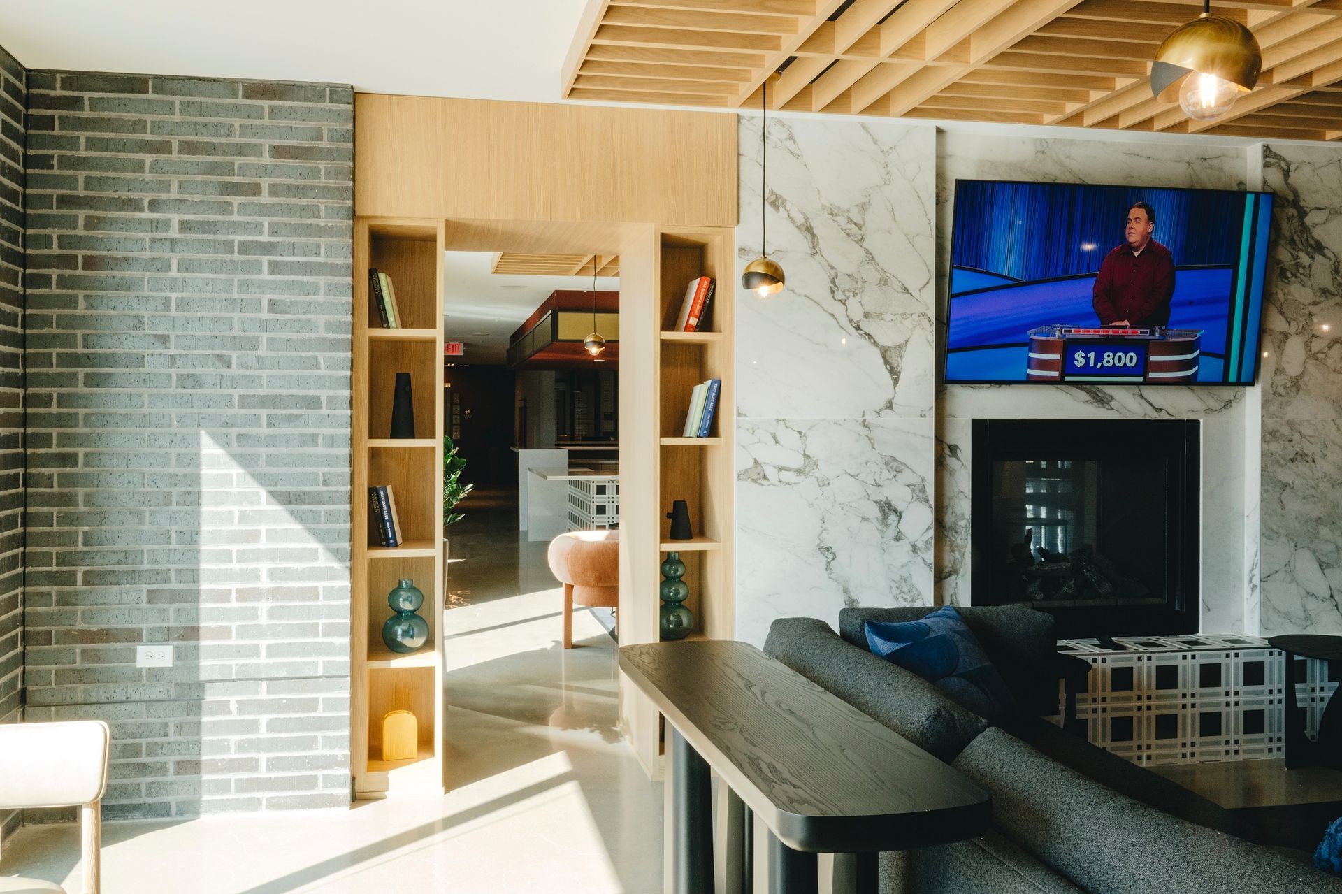 Modern living room with brick wall, marble fireplace, TV, and open doorway to the kitchen at Revelry in Madison, WI.