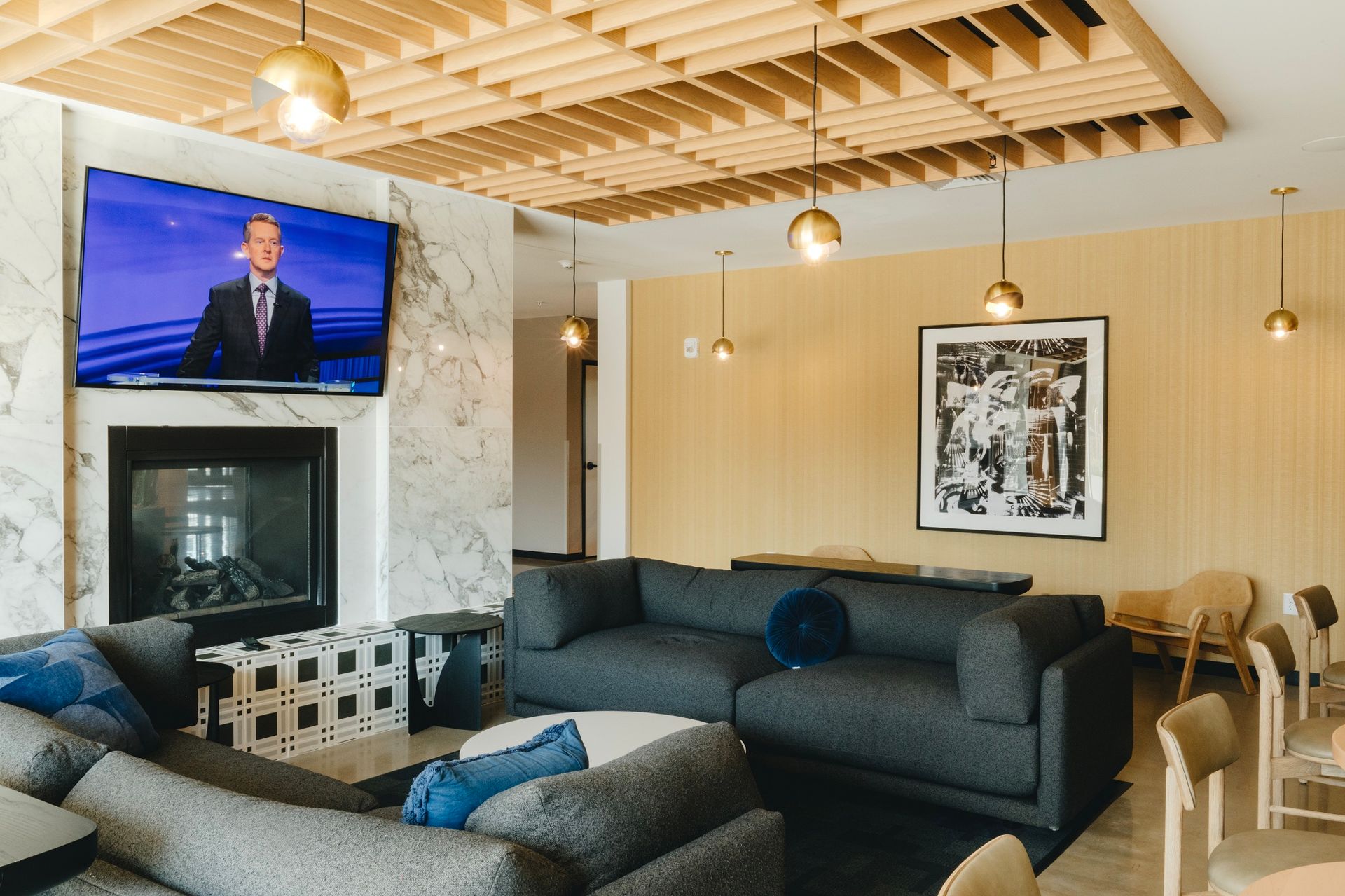 Lounge with TV over fireplace, sectional sofa, modern art, wood ceiling, and gold pendant lights at Revelry in Madison, WI.