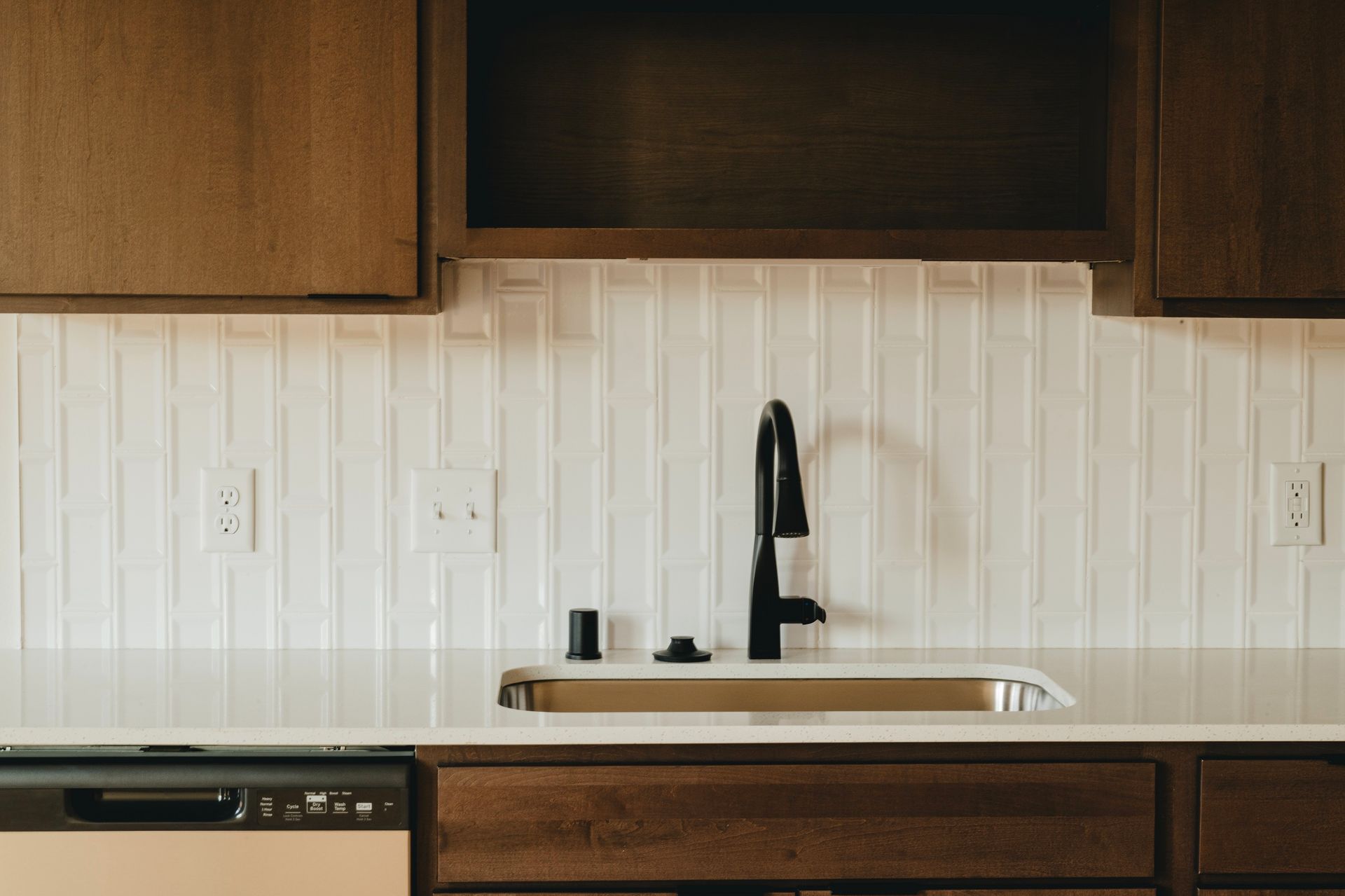 Kitchen with white backsplash, dark faucet, and wooden cabinets.