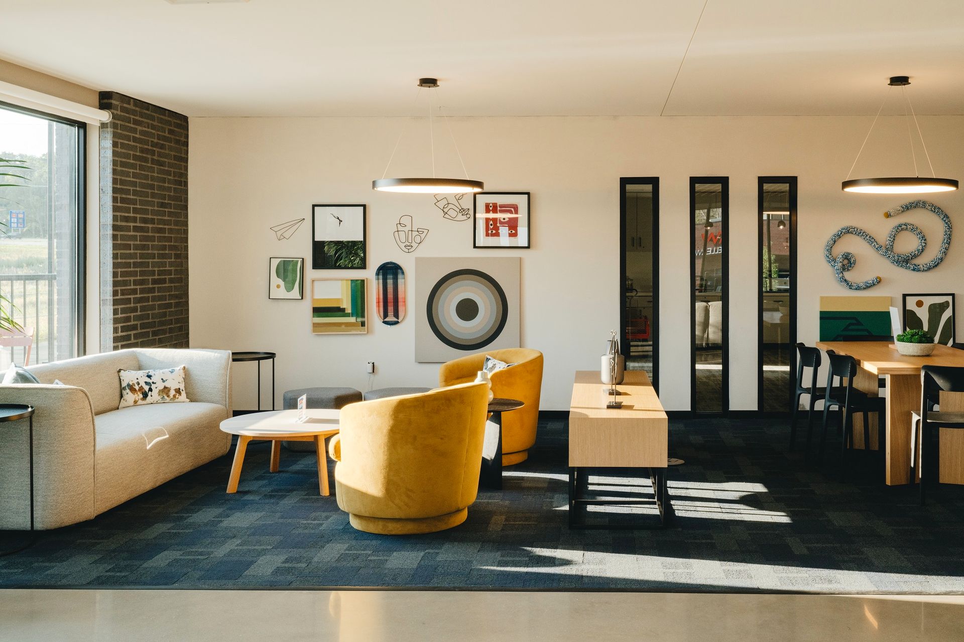 Modern living room with beige sofa, two yellow armchairs, artwork, and a dining table at Revelry in Madison, WI.