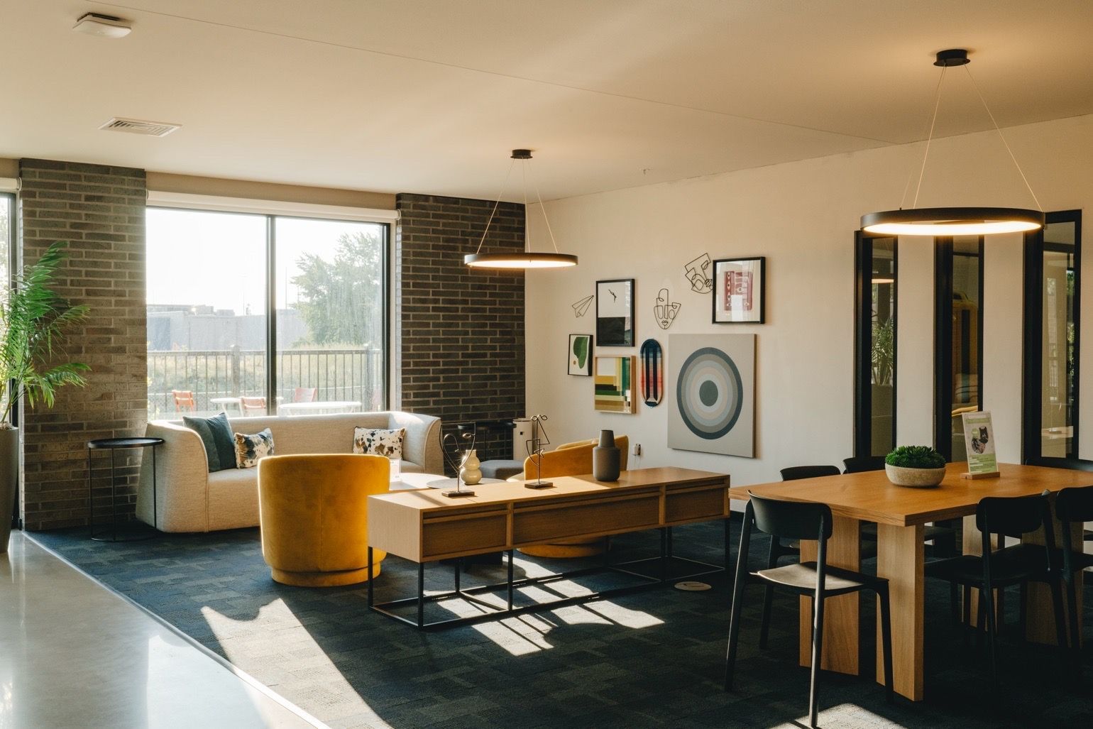 A modern lounge area with a sofa, art, and dining table under circular pendant lights; brick accent wall at Revelry in Madison, WI.