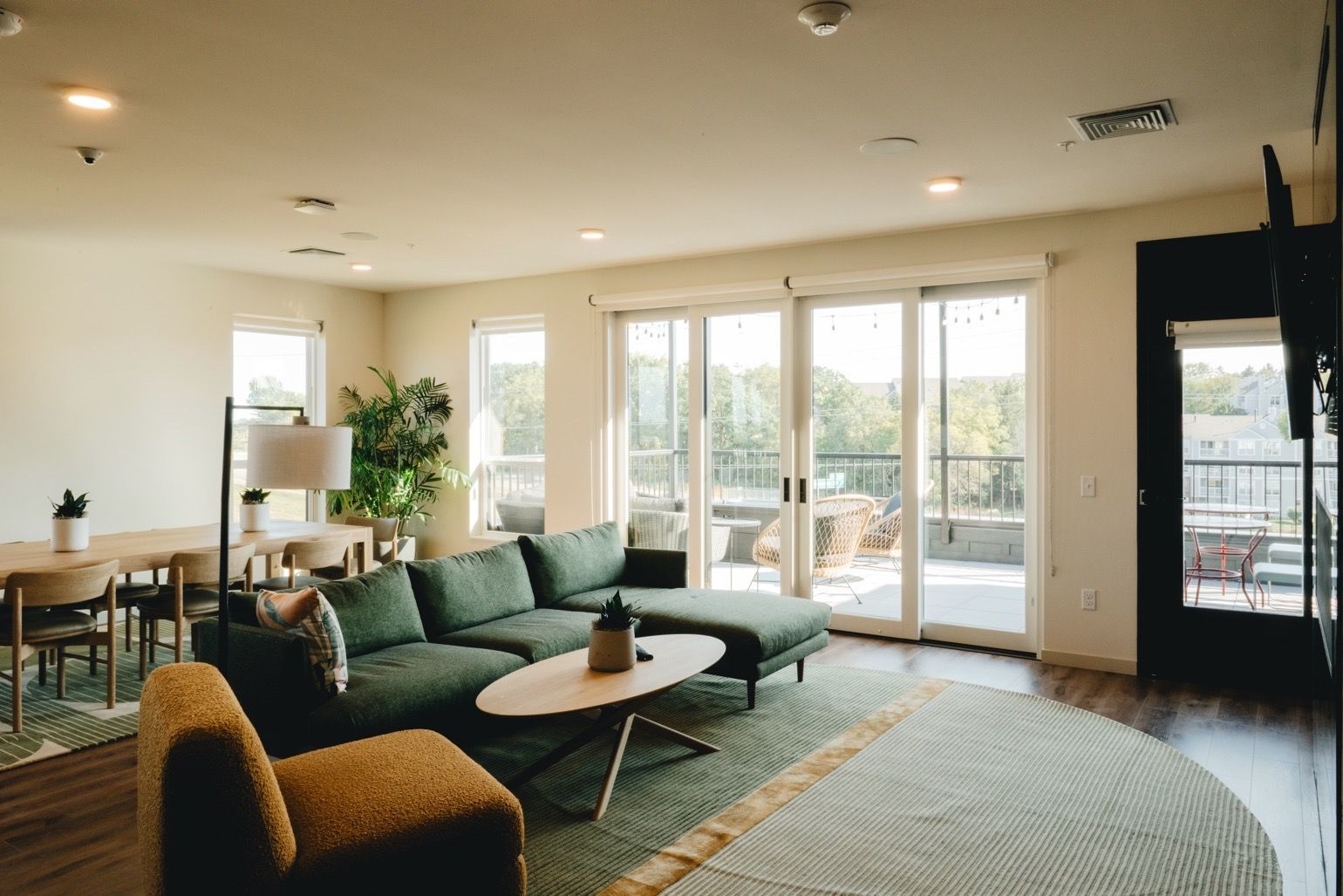 Spacious living room with green sectional sofa, large windows, and access to a balcony at Revelry in Madison, WI.
