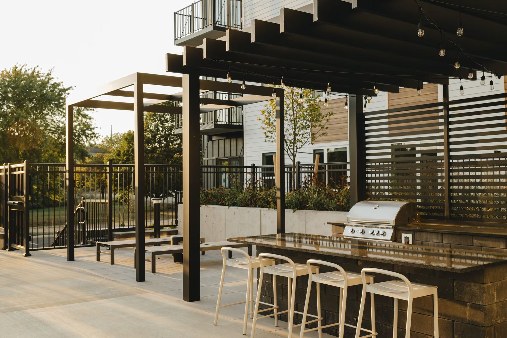 Outdoor grilling area with pergola, bar seating, and a view of an apartment building at Revelry in Madison, WI.