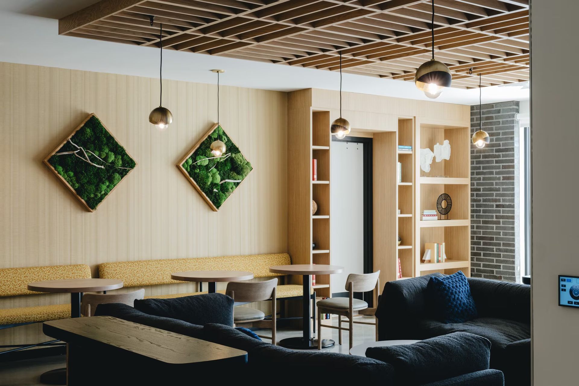 Modern lounge with built-in seating, moss art, hanging lights, and bookshelves at Revelry in Madison, WI.