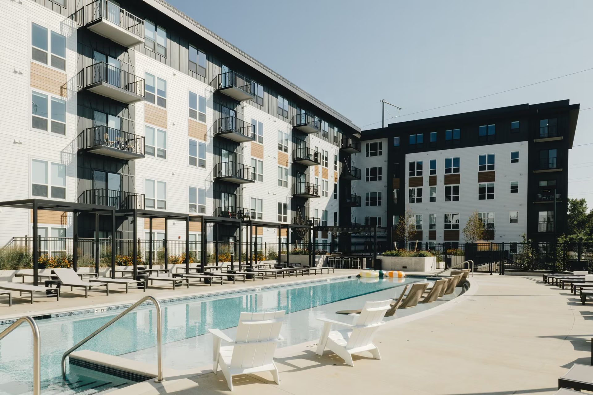 Apartment complex with a pool, lounge chairs, and balconies. Sunny day, modern architecture at Revelry in Madison, WI.