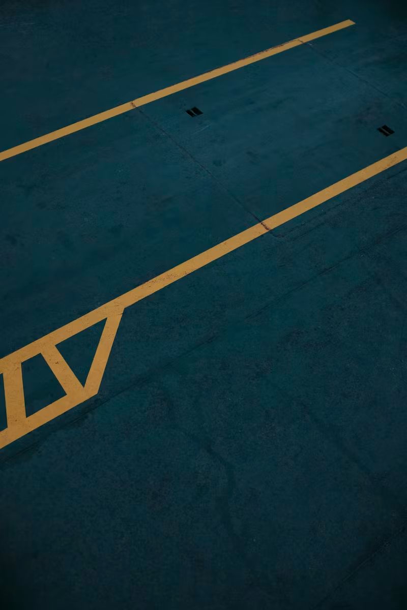 Blue parking lot pavement with yellow lane lines and a striped marking.