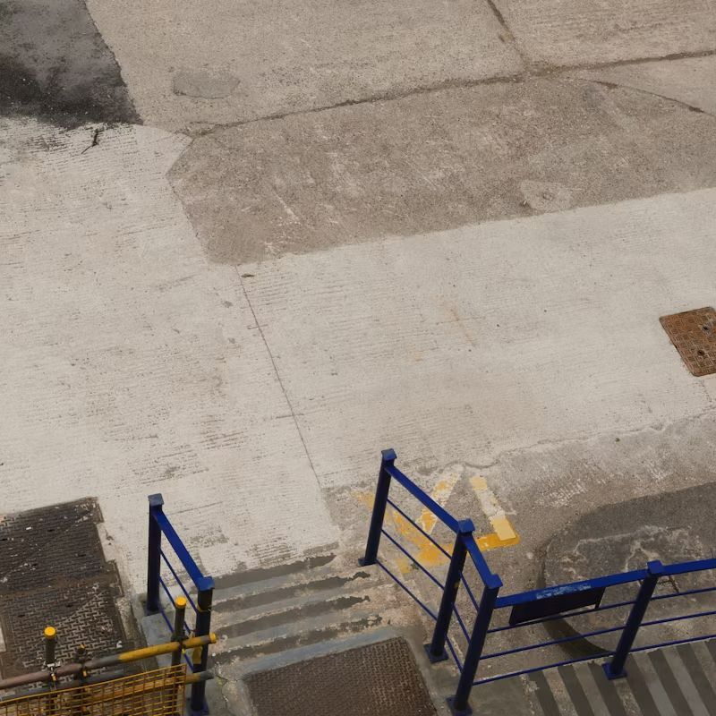 Blue metal stair railings beside concrete steps on a paved outdoor landing