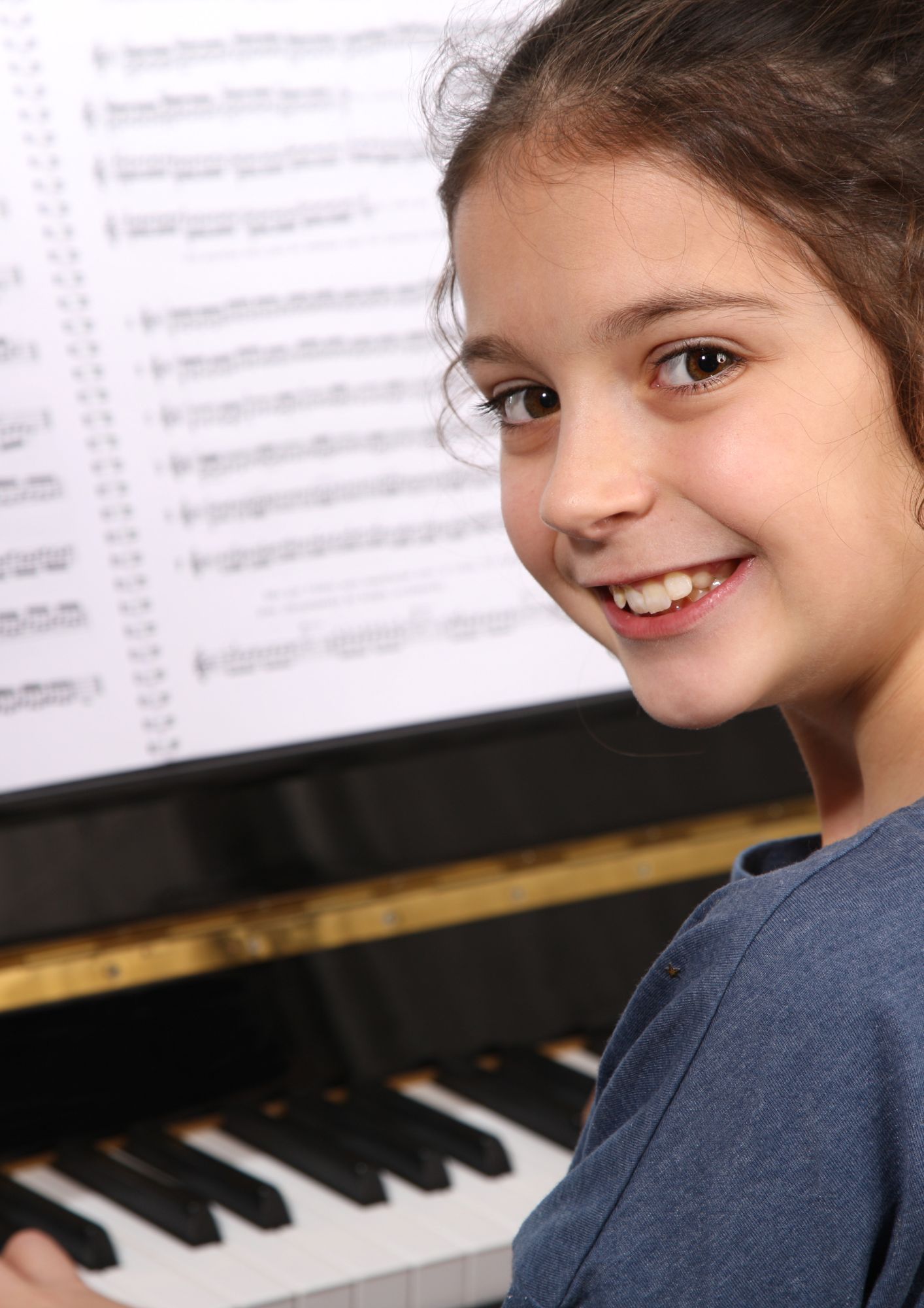 A young girl is playing a piano and smiling at the camera.