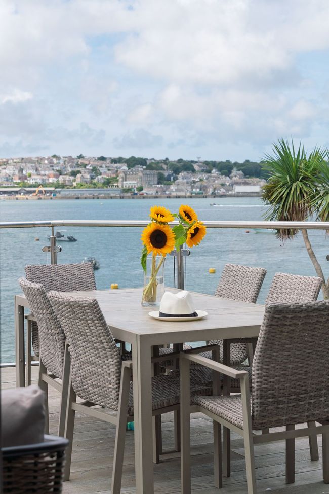 Patio table with sunflowers overlooking a calm waterfront and distant houses