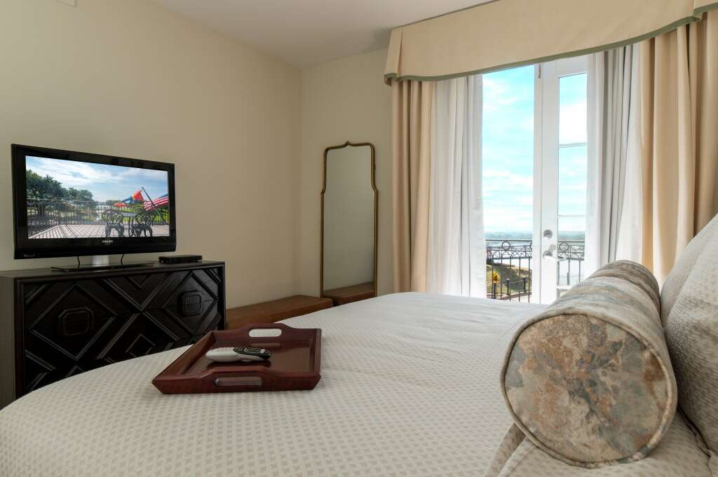 Bedroom with bed, TV, ornate dresser, large mirror, and balcony doors.