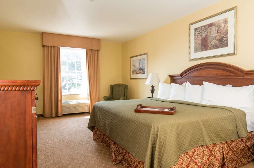 Hotel bedroom with king-size bed, window, arm chair, and artwork on yellow walls.