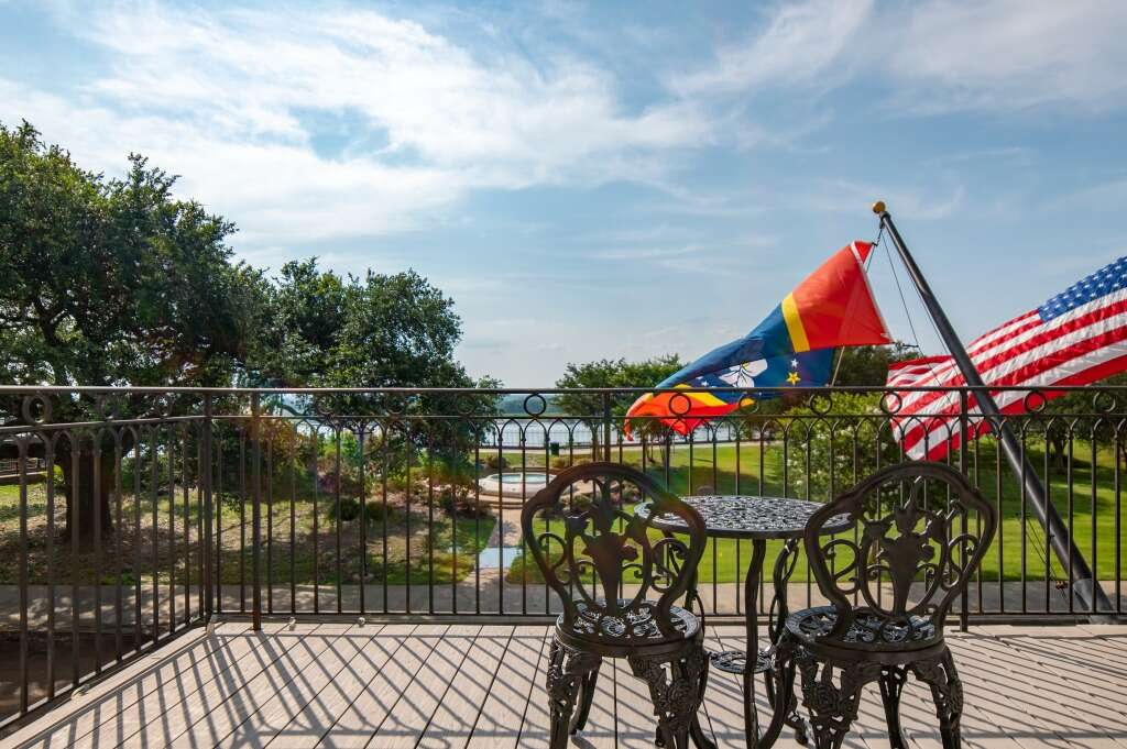 Patio with two ornate chairs, small table, flags, and a waterfront view on a sunny day.